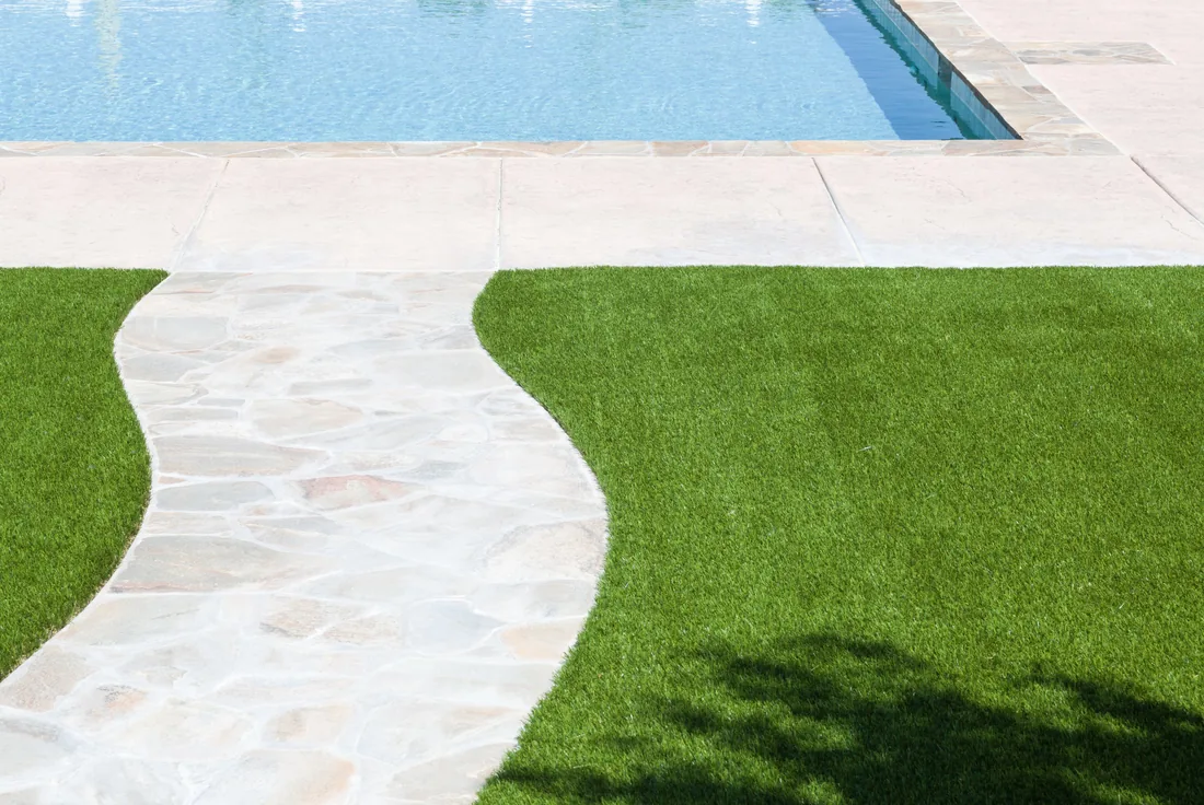 Synthetic turf finished neatly against pool coping beside a curved stone paved edge